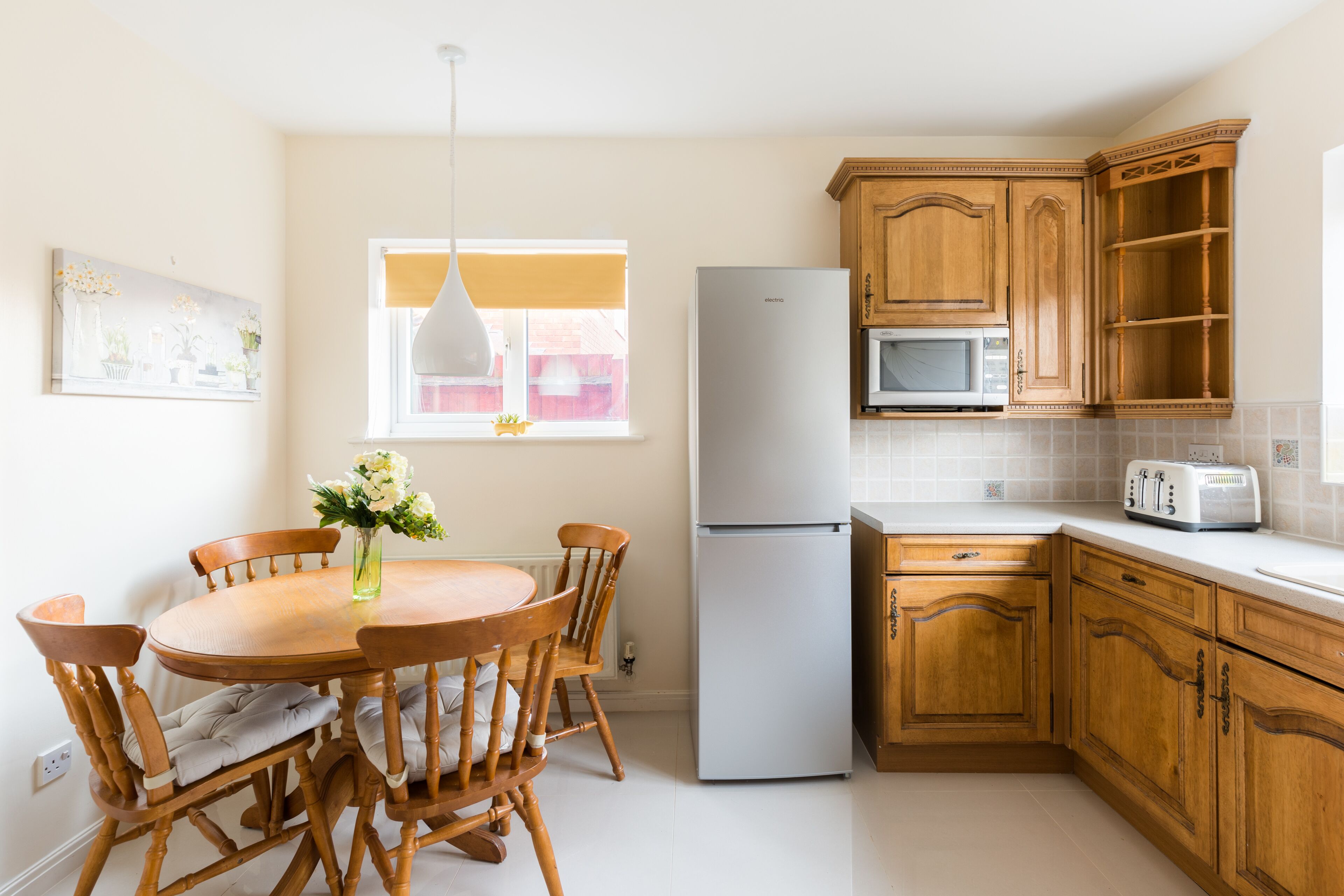 A kitchen with wooden cabinets, a white refrigerator, a microwave, and a dining table with chairs.