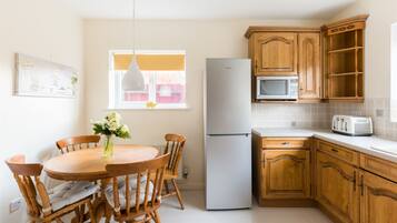 A kitchen with wooden cabinets, a white refrigerator, a microwave, and a dining table with chairs.