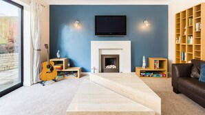 A living room with a fireplace, a television mounted above it, and a bookshelf filled with books.