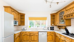 A kitchen with wooden cabinets, a white refrigerator, a dishwasher, and a window with a view of greenery.