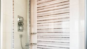 A glass-enclosed shower with a rain showerhead and a handheld showerhead, a glass door, and a tiled wall with horizontal lines.