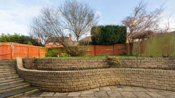 A brick garden with a curved stone wall, steps leading up to a raised bed, and a wooden fence.