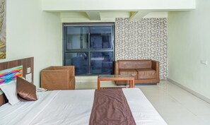 Una camera d'albergo con un letto, un comodino in legno, un tavolino, un divano e una grande finestra.