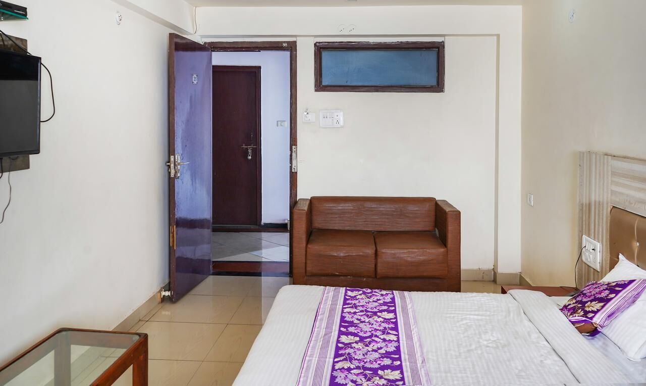A hotel room with a bed, a wooden bench, a television, and a door leading to another room.