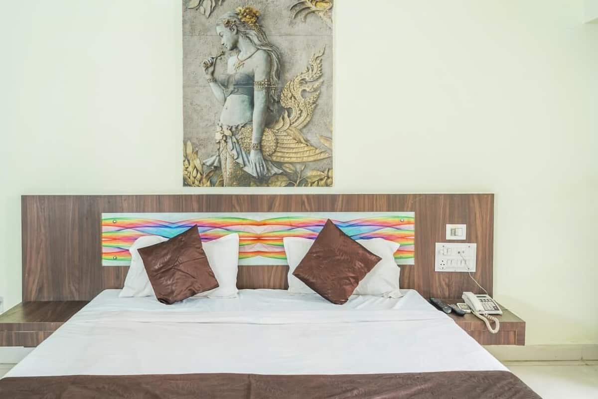 A bedroom with a bed, pillows, a nightstand, a phone, and a wall-mounted artwork.