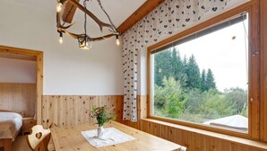 A wooden room with a large window, a wooden table with chairs, and a bed with a white headboard. - Alpine Hut in Eberstein Near Ski Area (Eberstein)