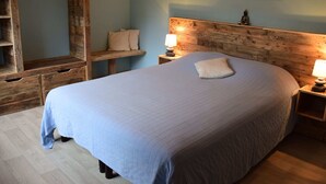 A bedroom with a wooden headboard, a bed with a quilted cover, two bedside lamps, a wooden bench, a wall-mounted shelf, and a hanging rack. - A Villa Between the Town Centre and the Forest (Spa)