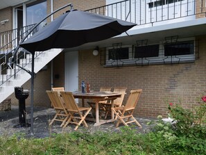 An outdoor patio with a table and chairs, a black umbrella, and a brick building in the background. - A Villa Between the Town Centre and the Forest (Spa)