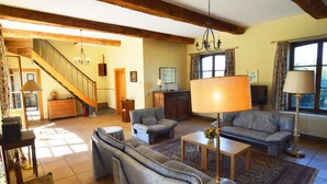 A spacious living room with a staircase, leather sofas, a chandelier, and a large window with curtains. - Cottage With Tennis Court (Havelange)