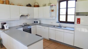A kitchen with white cabinets, a microwave, a stove, a sink, and a window with blinds. - Cottage With Tennis Court (Havelange)