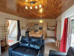 A modern kitchen with wooden cabinets, a dining table, and a black leather sofa.