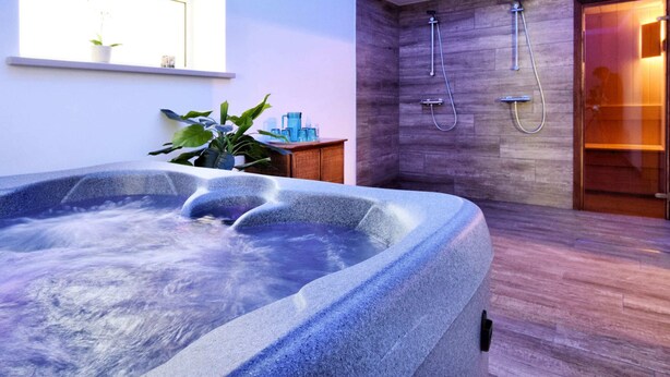 Ein modernes Badezimmer mit einer Stein-Whirlpool-Badewanne, Holzboden und einer Duschkabine.