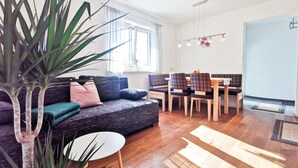 A modern living room with a sofa, dining table, chairs, and a large plant.