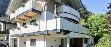 A modern two-story house with a balcony, outdoor seating, and a garden area.