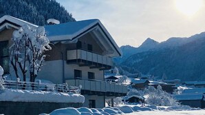 A modern building with a balcony, surrounded by snow-covered trees and mountains in the background.