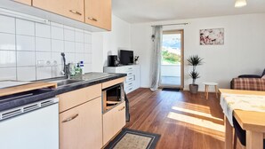A modern kitchen with white cabinets, a built-in oven, and a coffee maker. There is a dining area with a wooden table and chairs, and a small potted plant.