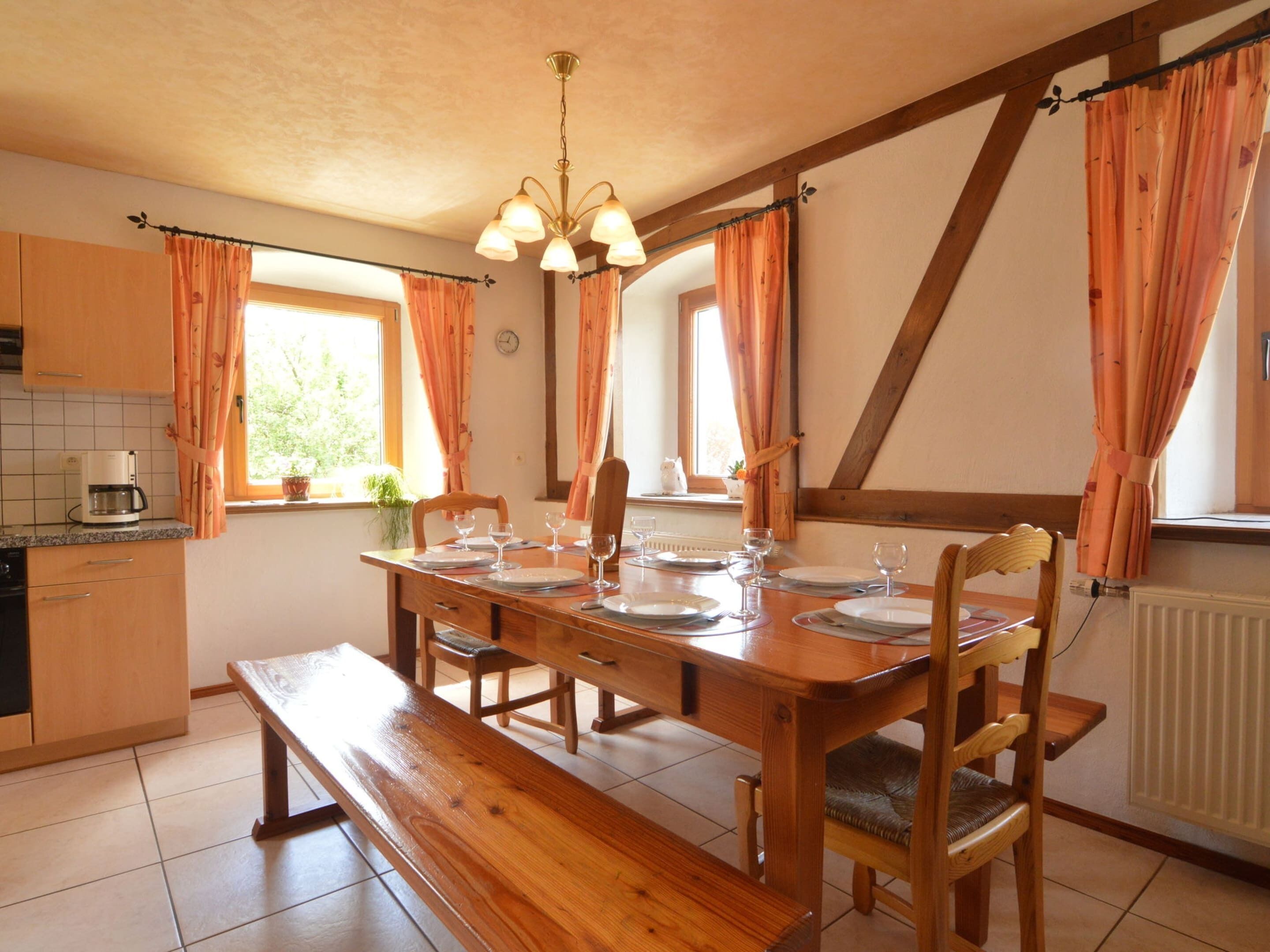 A dining area with a wooden table set for four, a bench, and wooden chairs.