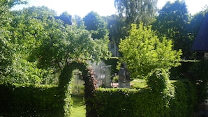 A lush garden with a statue, a greenhouse, and a building in the background. - Holiday Home in Butgenbach Near the Lake (Buetgenbach)