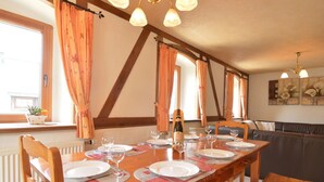 A dining area with a long wooden table set for six, flanked by wooden chairs. A bottle of champagne is on the table, and the room has a rustic charm with exposed wooden beams and a radiator. - Holiday Home in Butgenbach Near the Lake (Buetgenbach)