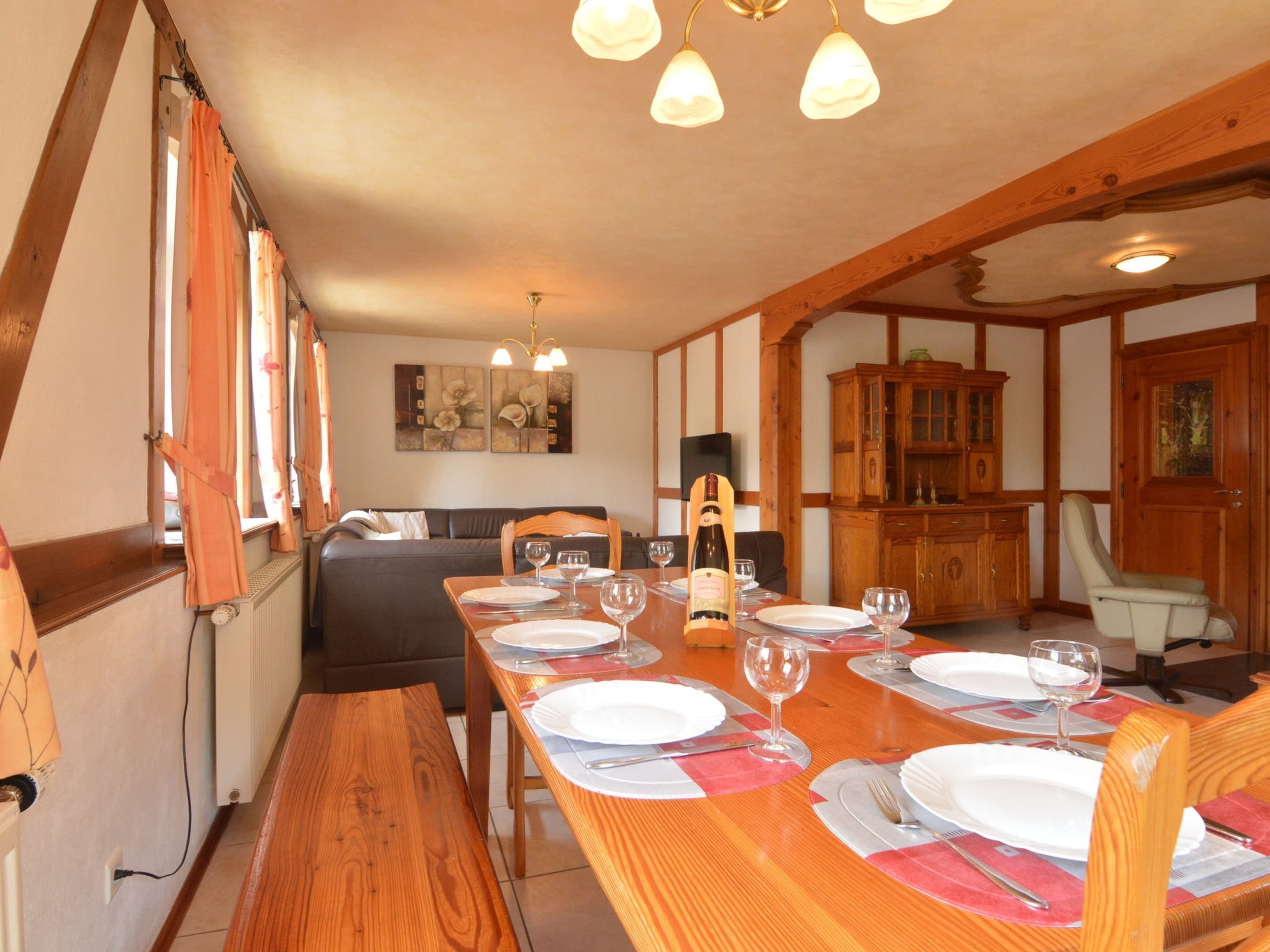 Un coin repas avec une table en bois dressée pour quatre personnes, un canapé en arrière-plan et un meuble en bois.