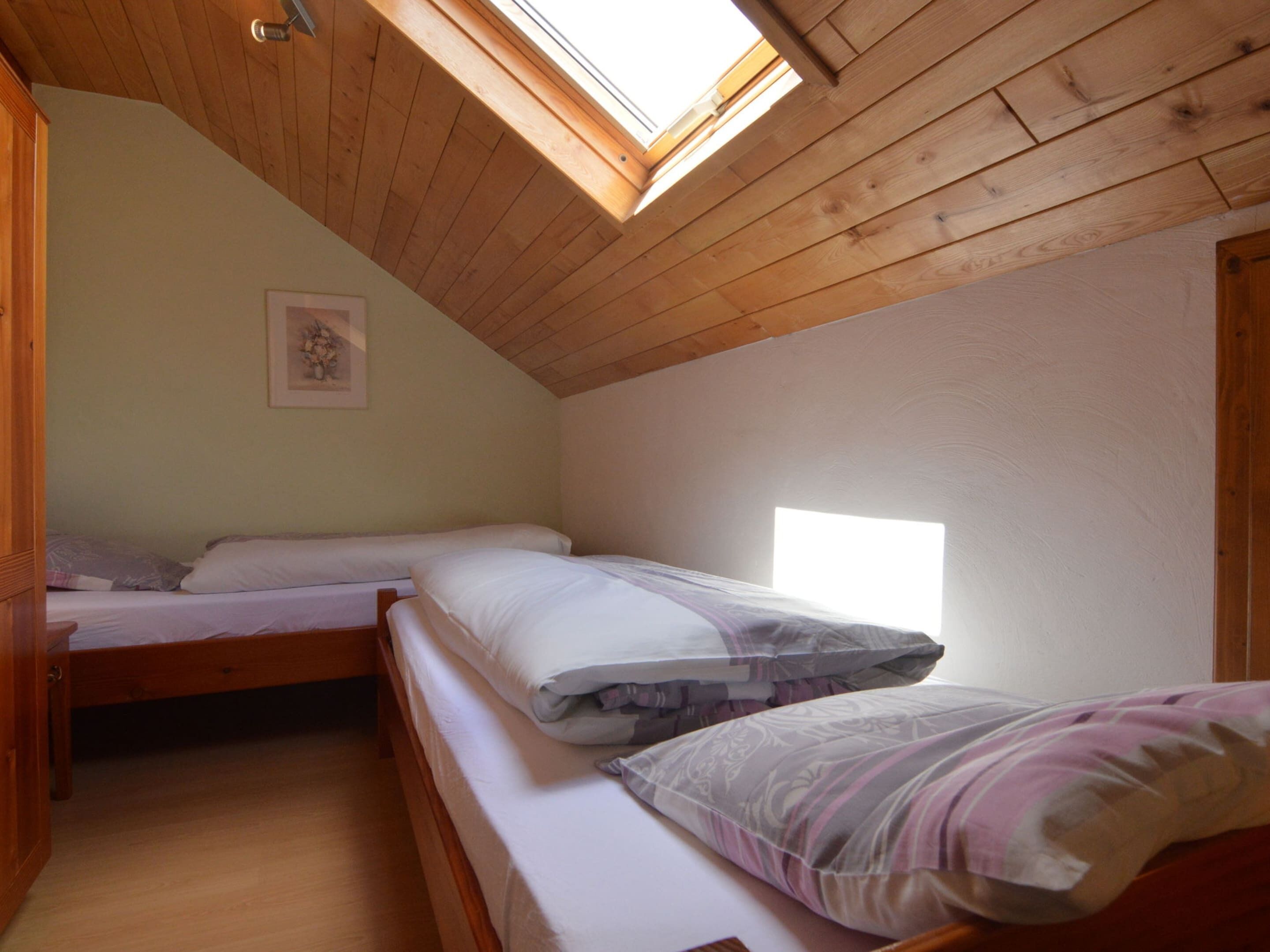 Una piccola e accogliente camera da letto con due letti, travi in legno al soffitto e un velux.