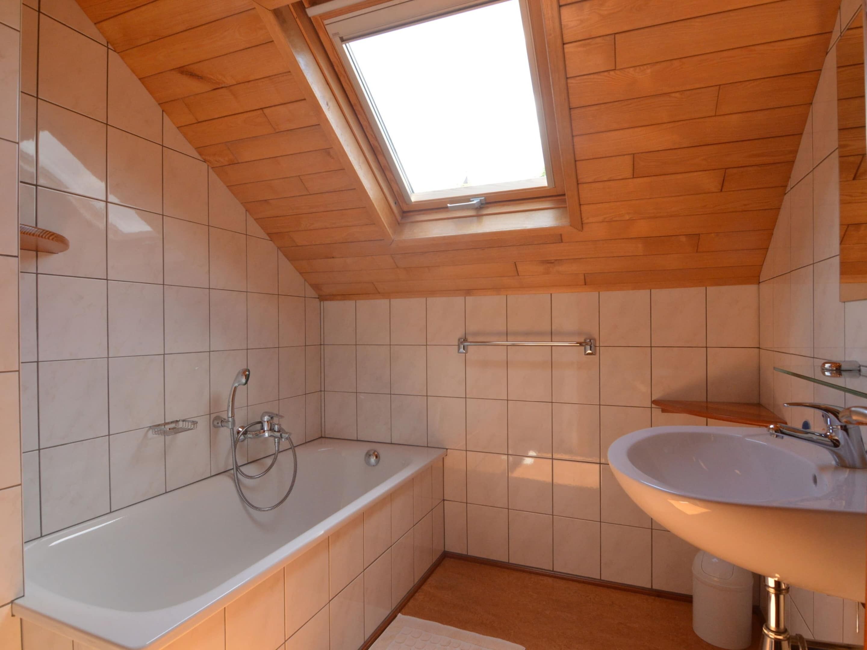 A modern bathroom with a skylight, a bathtub, a sink, and a towel rack.