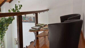 A room with a wooden ceiling, a view of a city street through a window, a table with books and papers, and a dark chair. - Nature Escape in Martelange (Martelange)