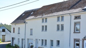 A two-story building with multiple windows and a tiled roof. There is a small garden area with potted plants and a water feature. - Nature Escape in Martelange (Martelange)