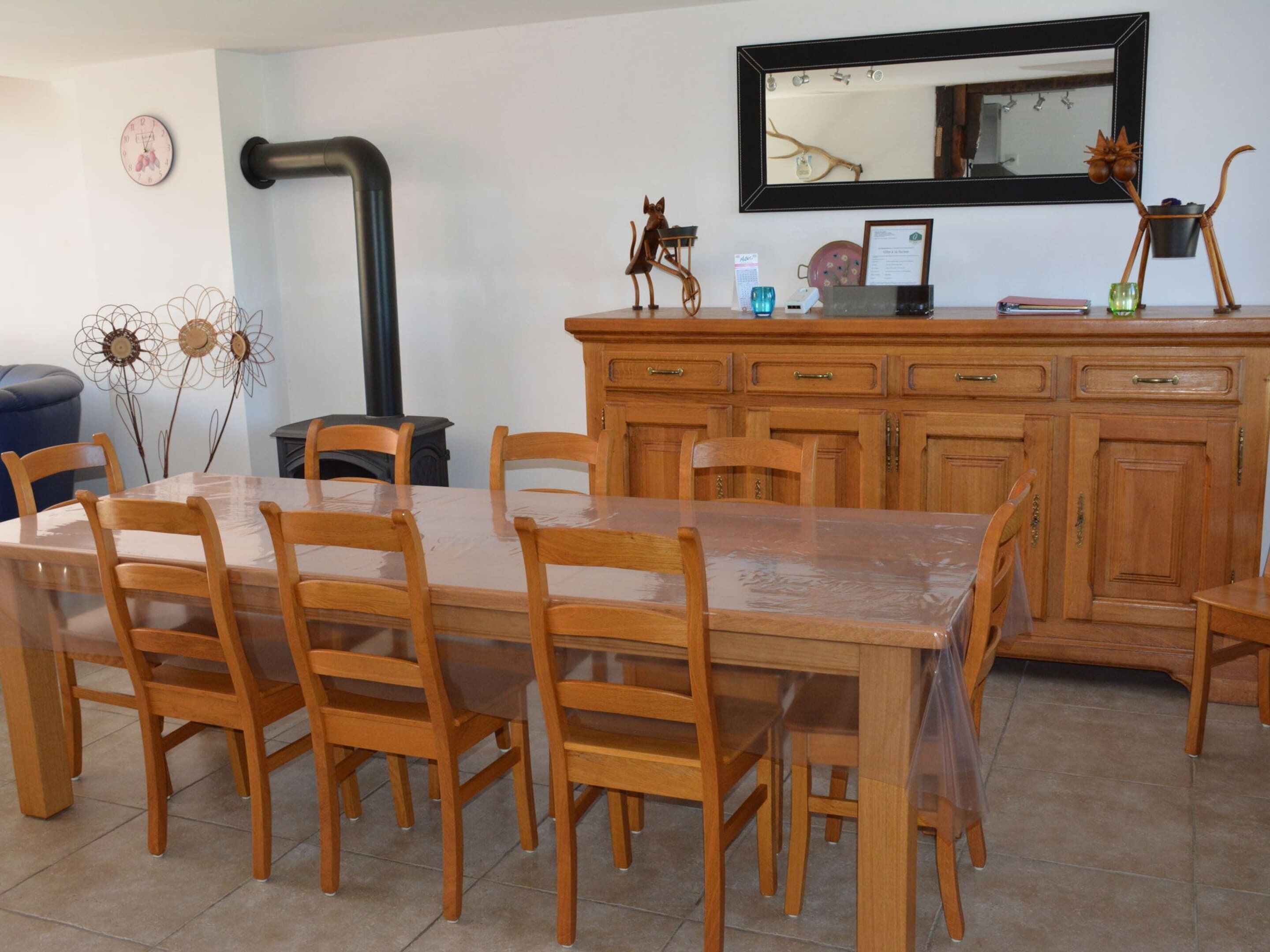 Un coin repas avec une table et des chaises en bois, une cuisine avec des meubles en bois, un tuyau noir et un miroir au mur.