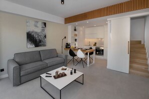 A modern living room with a grey sofa, a white coffee table, and a dining area with a wooden table and chairs.