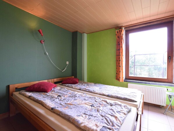 A room with two beds, a radiator, a window with curtains, and a wall-mounted lamp. - Quaint Cottage In Petite Langlire with Hot Tub (Gouvy)