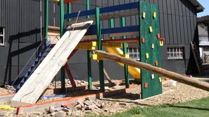 A playground with a slide and climbing structures in front of a building with a dark facade and windows. - Holiday Home in Burg Reuland (Burg-Reuland)