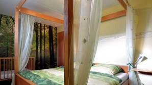 A four-poster bed with a forest mural backdrop, a wooden headboard, and a window with curtains. - Holiday Home in Burg Reuland (Burg-Reuland)