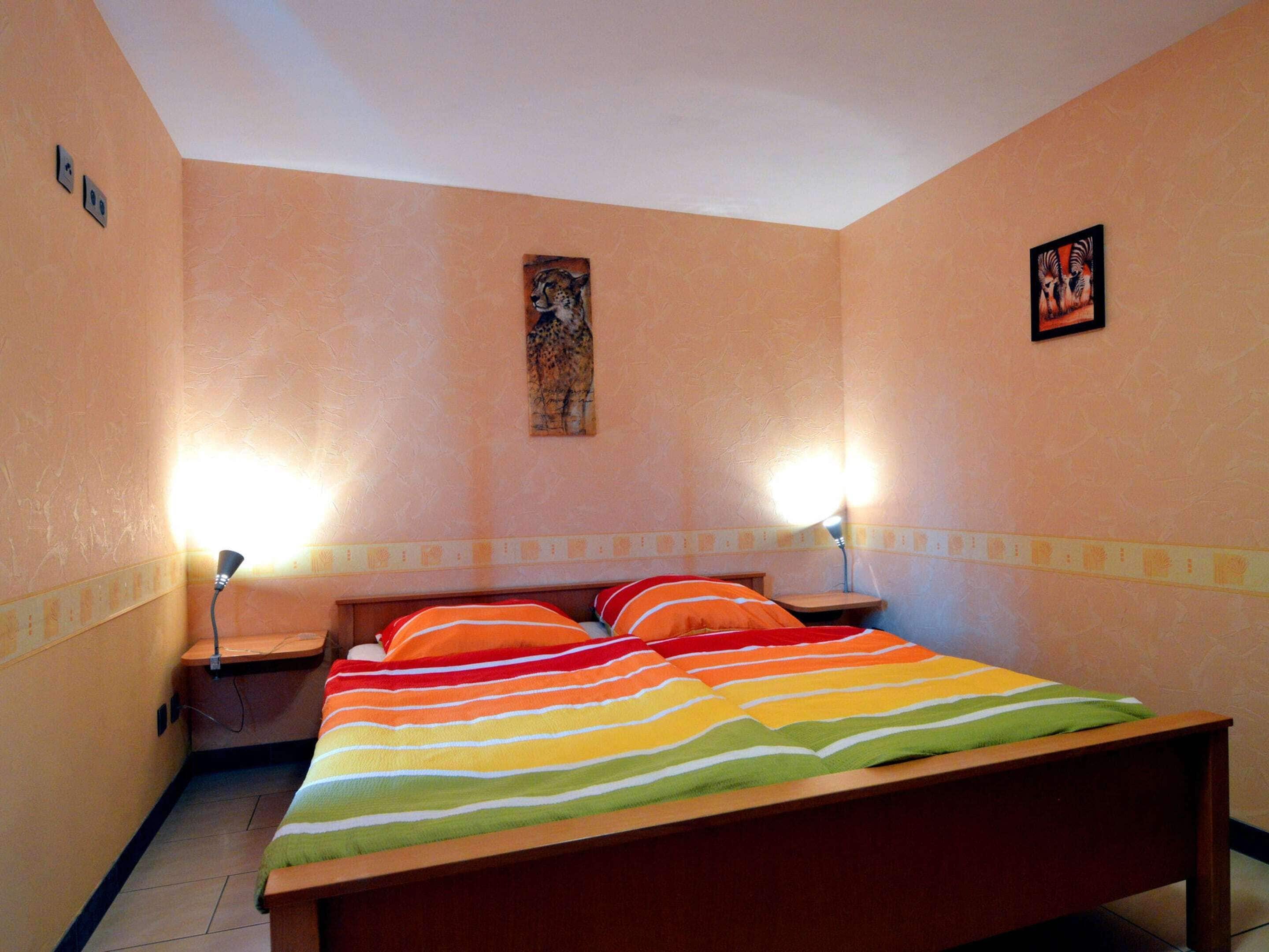 A bedroom with a bed, two bedside lamps, a nightstand, and two wall-mounted paintings.