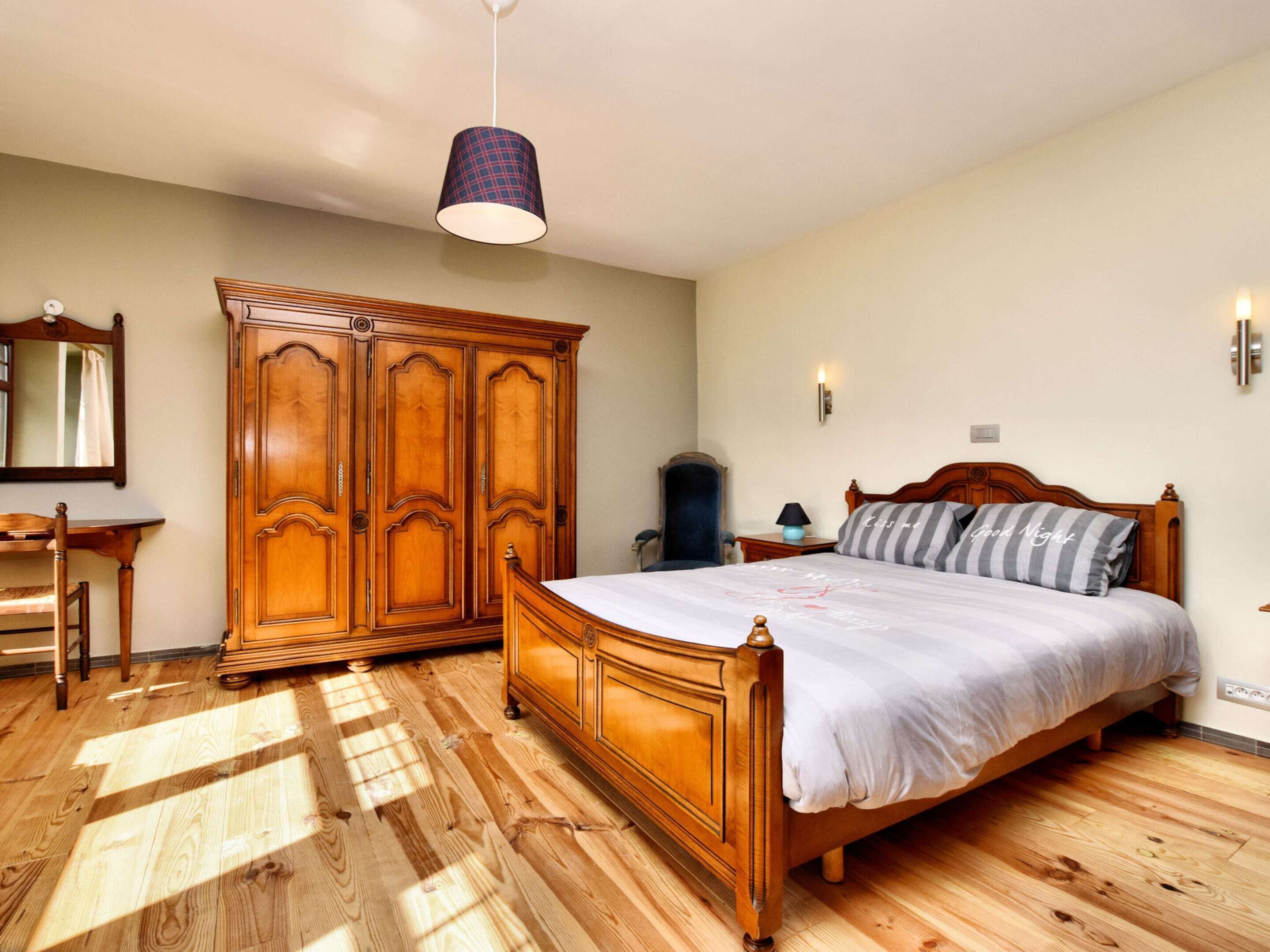 Une chambre à coucher avec un lit en bois, une armoire, un bureau et un miroir.