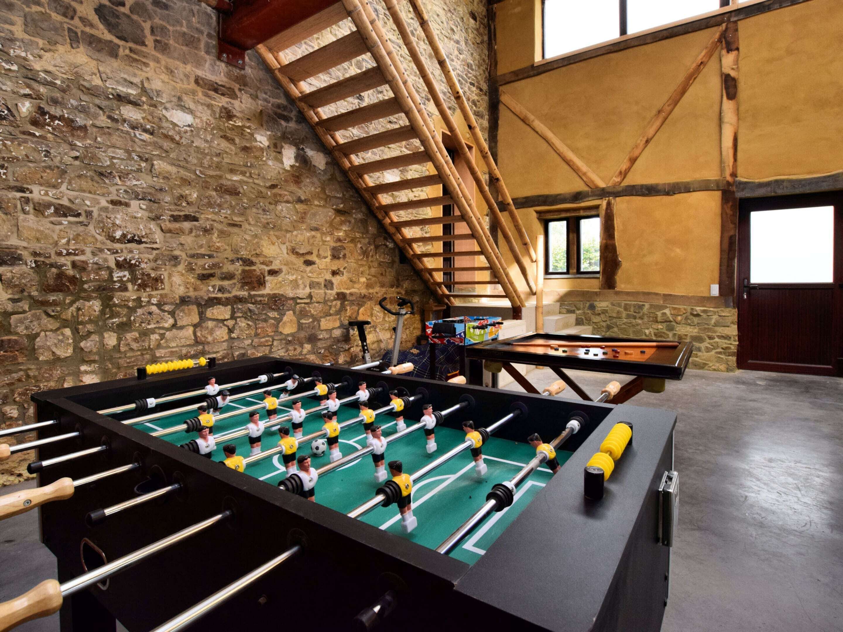 A foosball table in a room with stone walls and a wooden staircase.