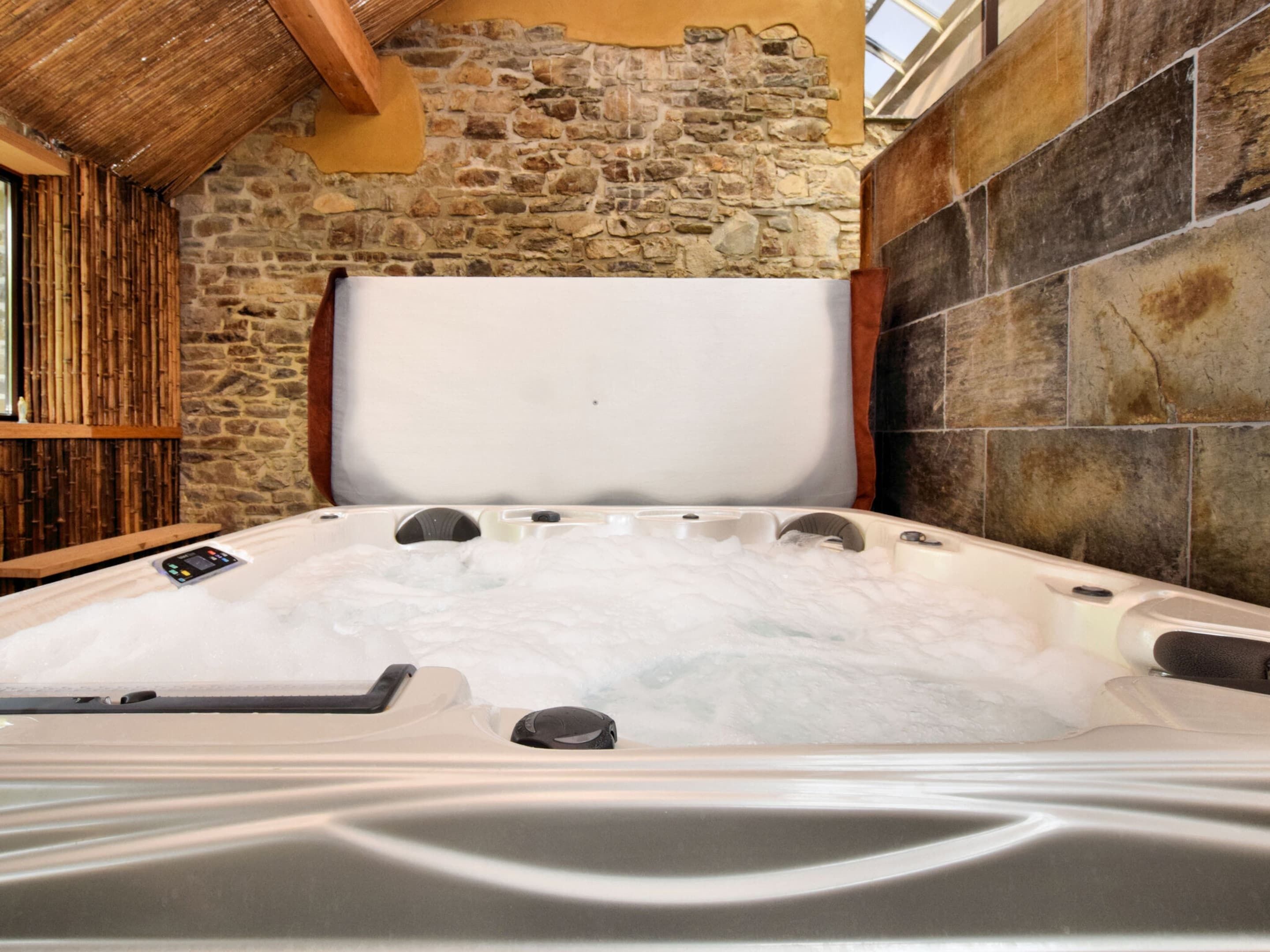 Un jacuzzi con un fondo de pared de piedra y una estructura de bambú.