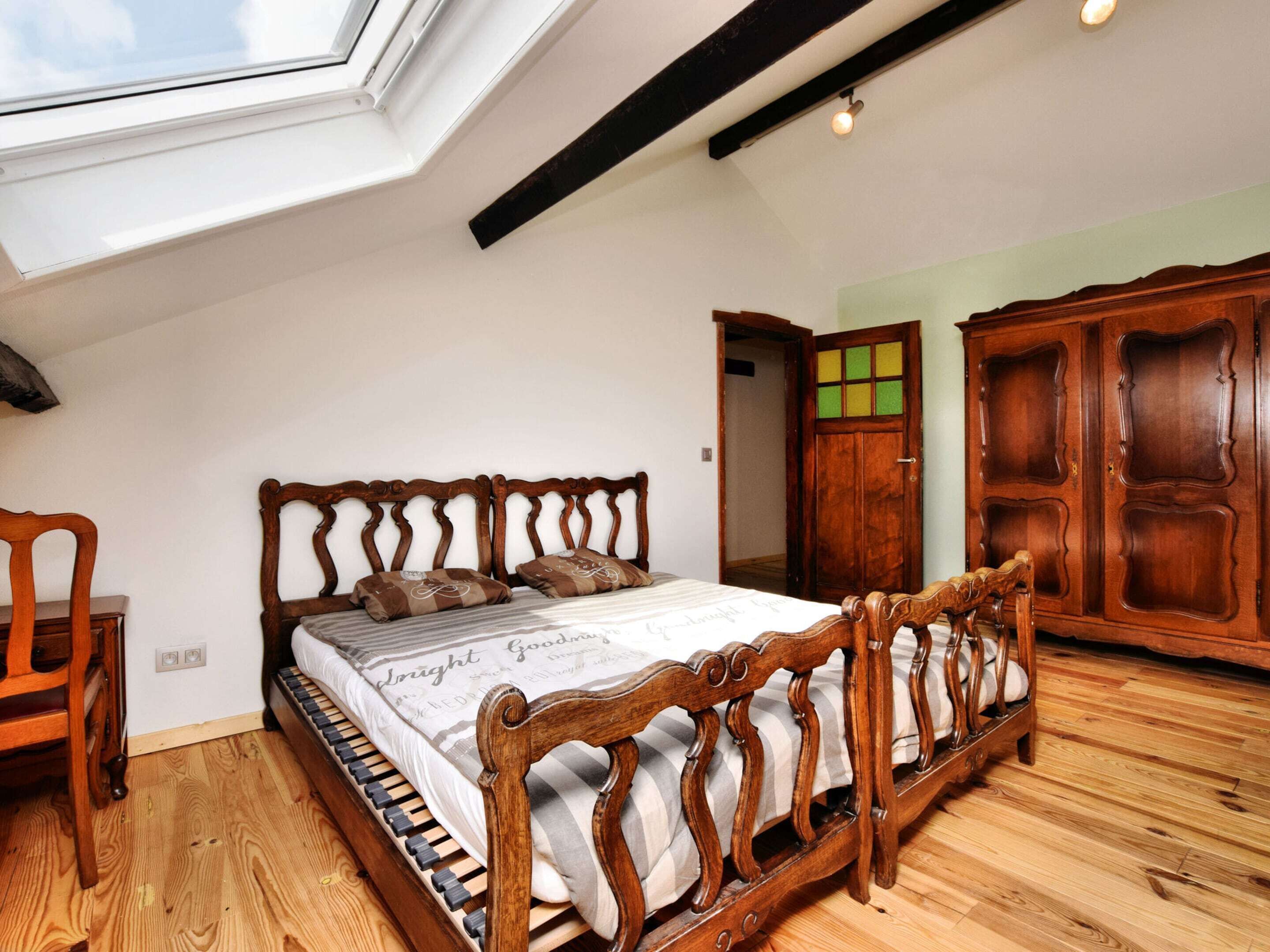 Ein Schlafzimmer mit Dachfenster, einem hölzernen Bett, einem Kleiderschrank und einer Tür mit grünem Fenster.