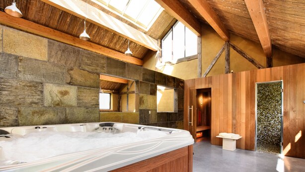 A modern bathroom with a large wooden bathtub, stone walls, and a skylight. - Pleasant Holiday Home in Erezée Ardennes with Hot Tub, Sauna (Erezee)