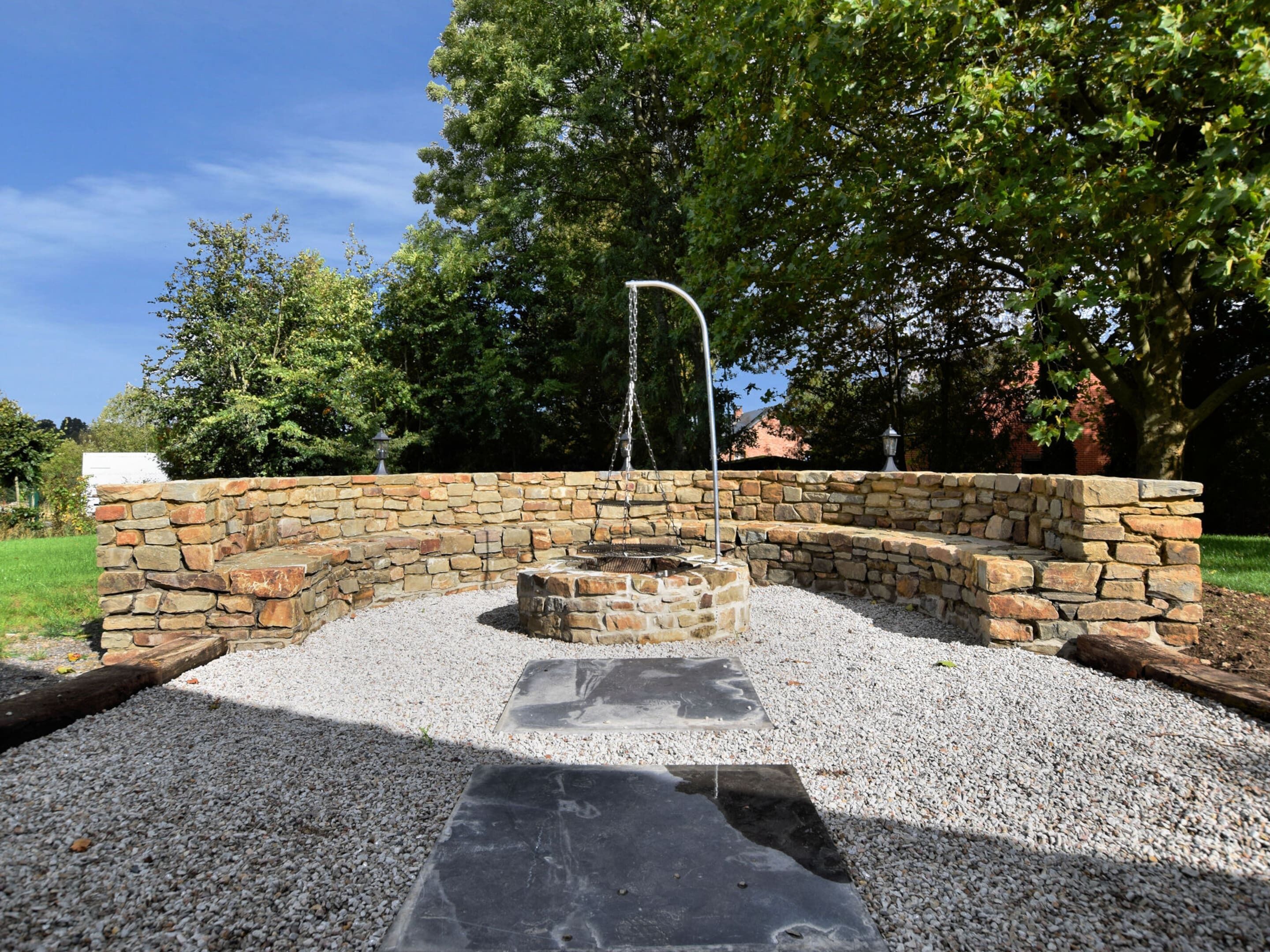 A stone fountain with a water feature, surrounded by a stone wall and gravel.