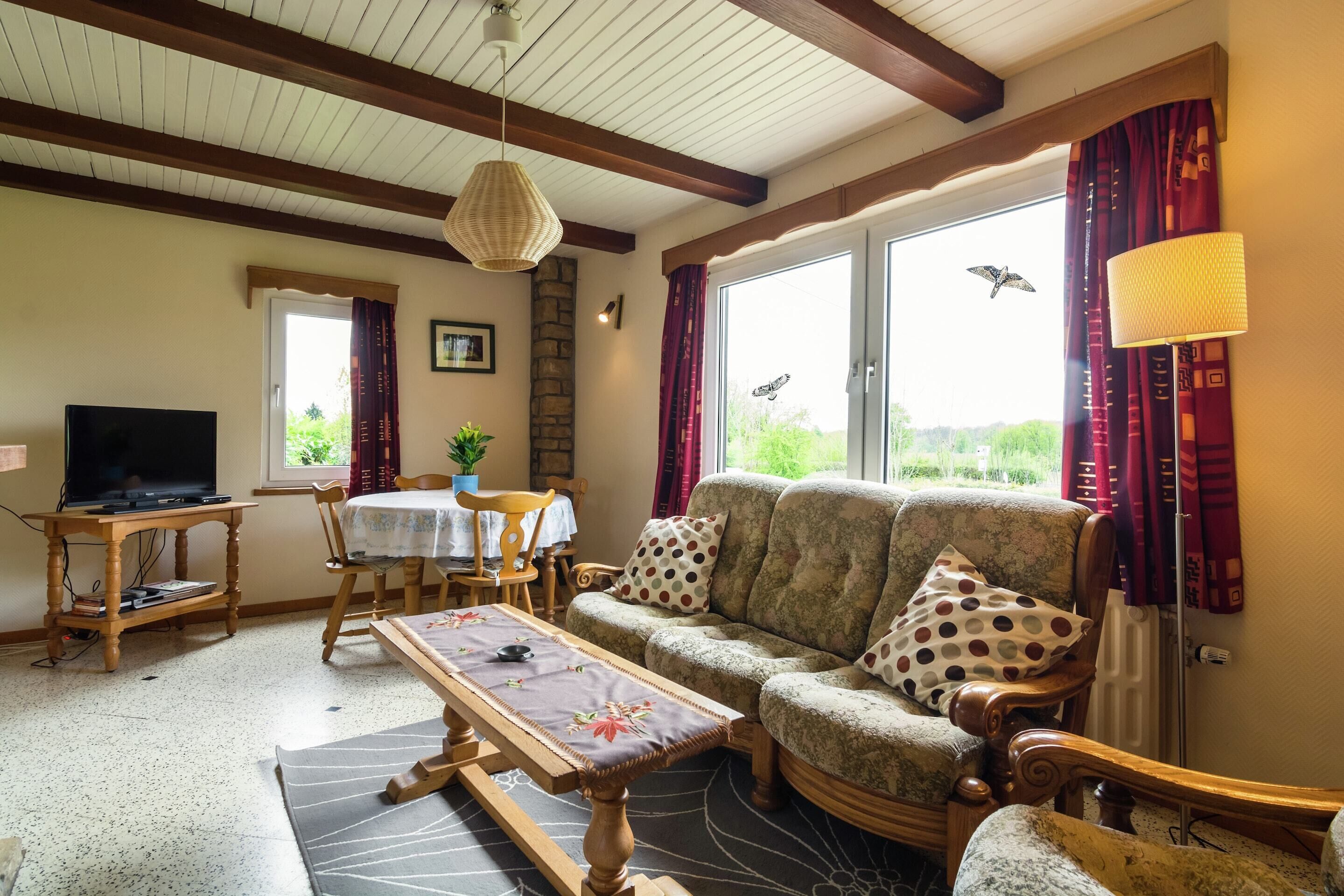 A living room with a sofa, a TV, a table, and a window with curtains.