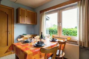 A dining area with a table set for four, a bottle of wine, and a window with a view of greenery. - Charming Cottage in Chiny (Chiny)