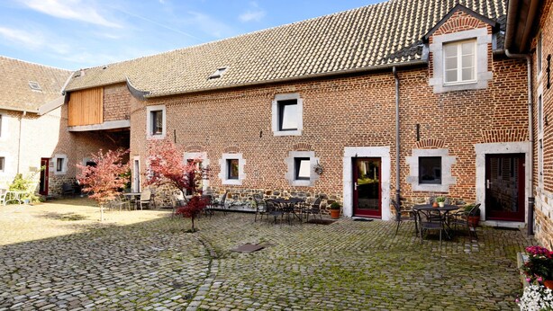 A courtyard with cobblestone paving, a brick building with multiple windows and doors, and outdoor seating with chairs and tables. - Nice Apartments in a Monumental Square Farm (Vise)