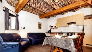 A cozy living area with a dining table set for four, a blue sofa, and a kitchen with white cabinets. - Nice Apartments in a Monumental Square Farm (Vise)