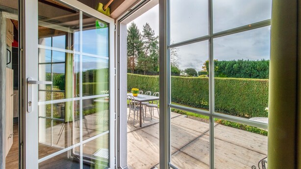 Une maison moderne avec une porte vitrée donnant sur un patio aménagé avec une table et des chaises.