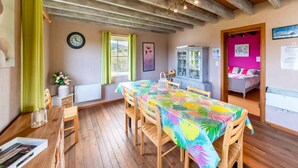 Une pièce avec un plafond en bois, une table à manger avec des chaises, un buffet, un lit et une fenêtre avec des rideaux.