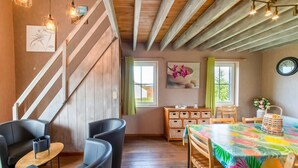 Une pièce avec un escalier en bois, une table à manger recouverte d’une nappe colorée et un buffet en bois avec des paniers.