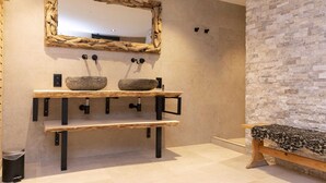 A bathroom with a stone sink, wooden shelves, a mirror with a natural frame, and a stone wall. - Cosy Chalet in Odeigne with Hot Tub (Manhay)