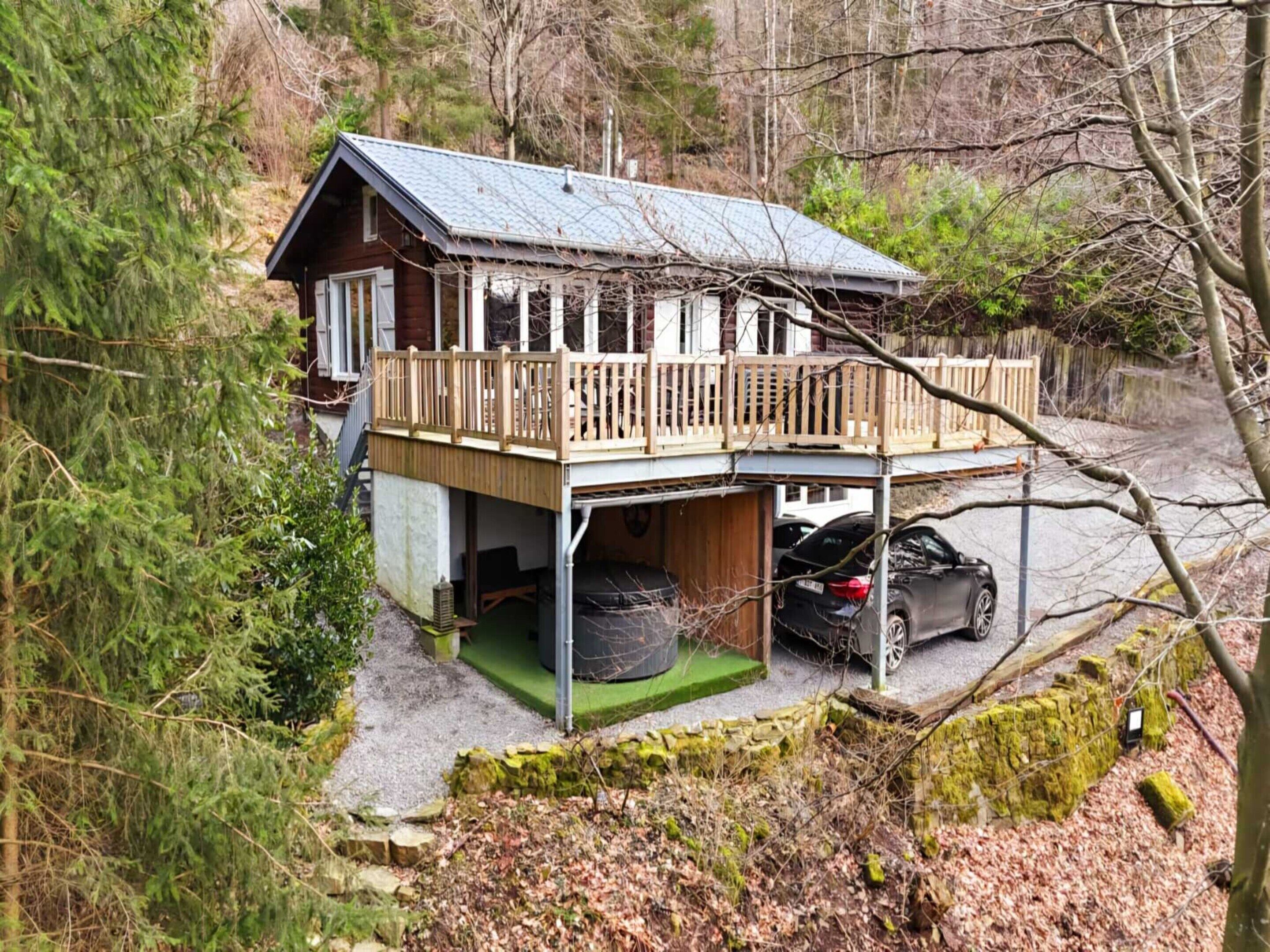 A cabin with a wooden deck and a car parked in front.