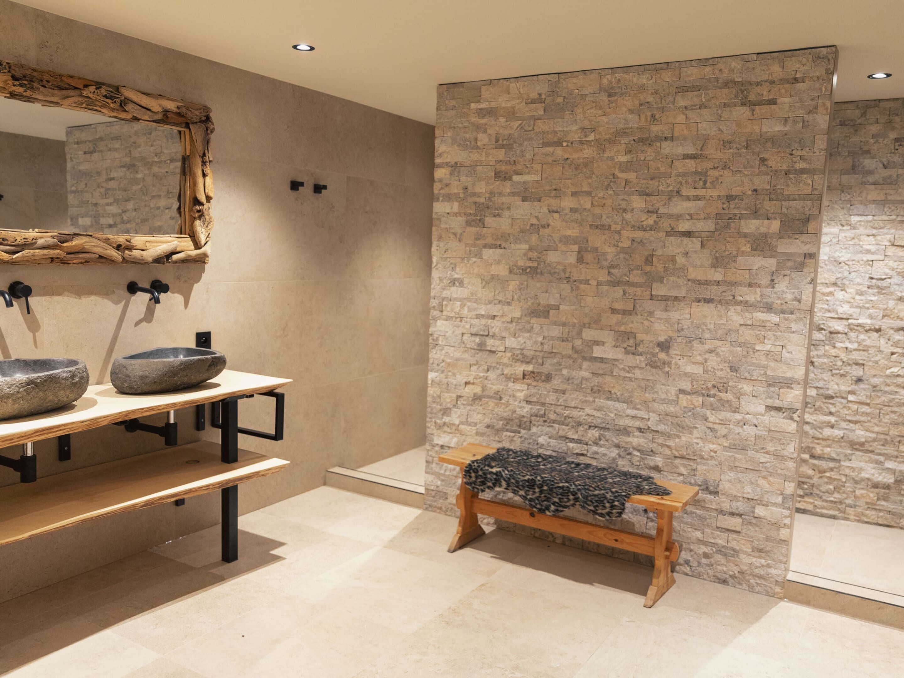 A bathroom with a stone wall, a wooden bench, and a mirror with a rustic frame.